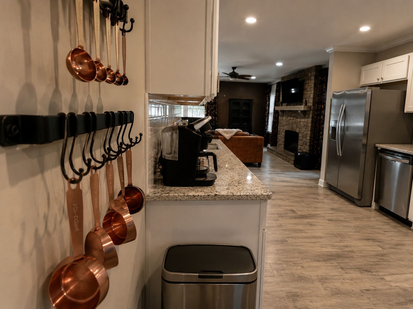 Una cocina moderna con electrodomésticos de acero inoxidable, encimera de granito y utensilios de cocina de cobre colgados en la pared.