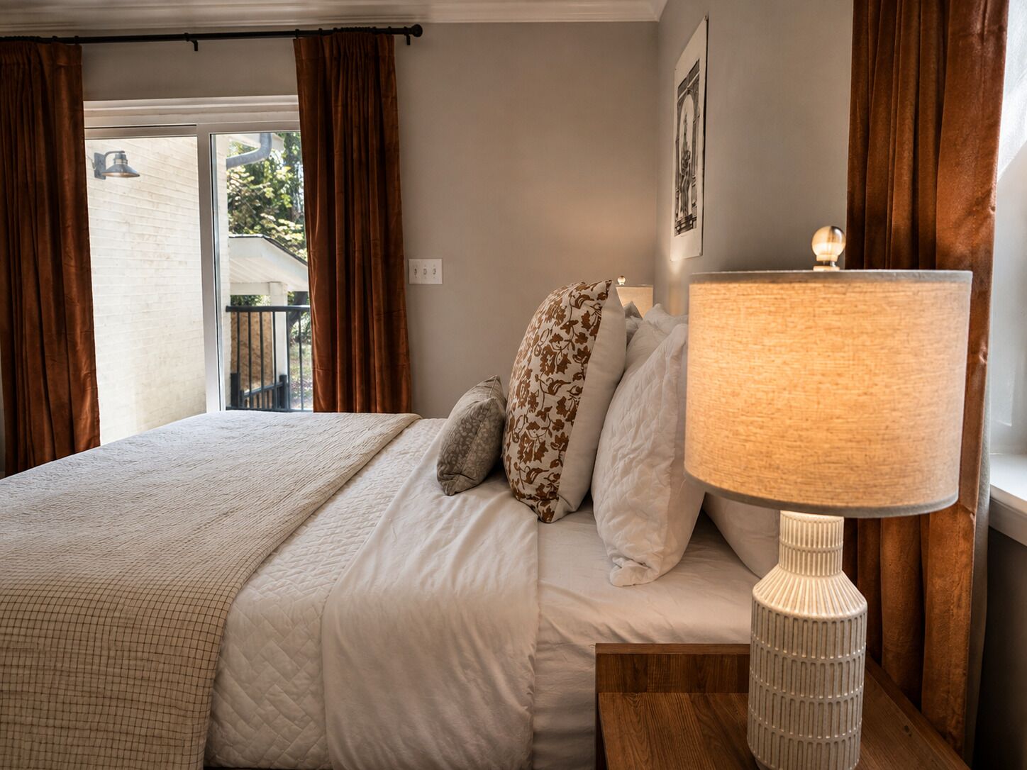 A hotel room with a bed, a bedside lamp, and a view of the outdoors.