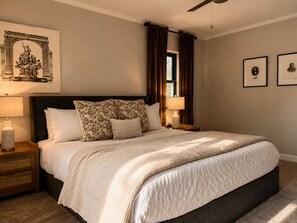 A bedroom with a large bed, two bedside tables, a ceiling fan, and a window with curtains. - Man cave, Office, Soaking tub, & Firepit. (Winston-Salem)