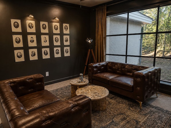 A room with a dark wall, a brown leather sofa, a round coffee table, and a large window with curtains.
