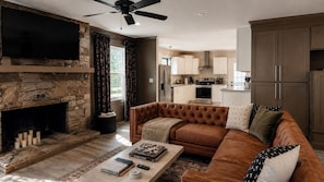 A living room with a stone fireplace, leather sofa, and a flat-screen TV.