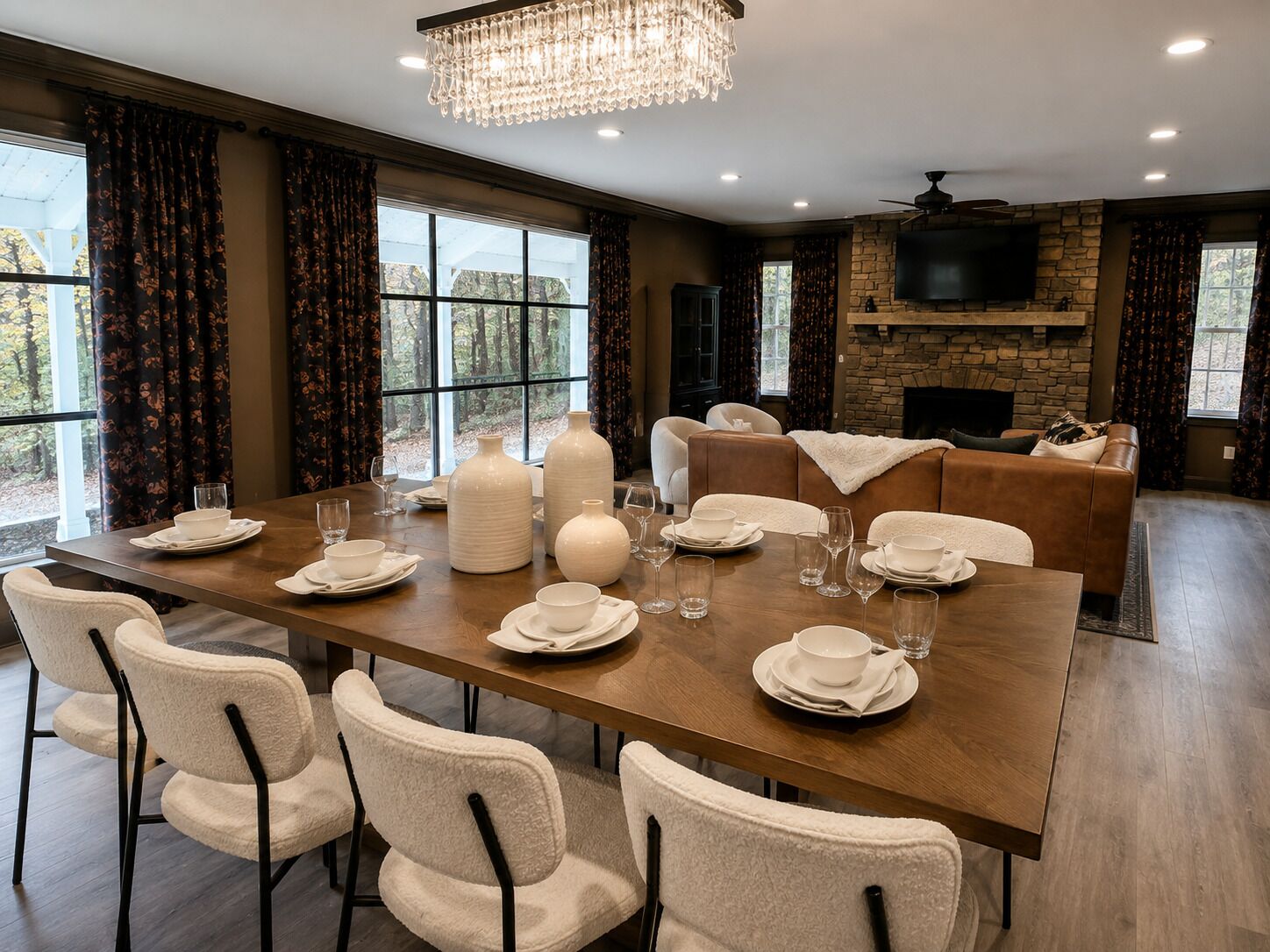 A dining area with a long table set for six, surrounded by chairs, with a fireplace and a television in the background.