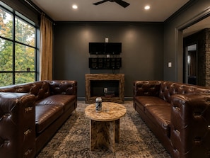 A room with two leather sofas, a round coffee table, a fireplace, and a mounted television.