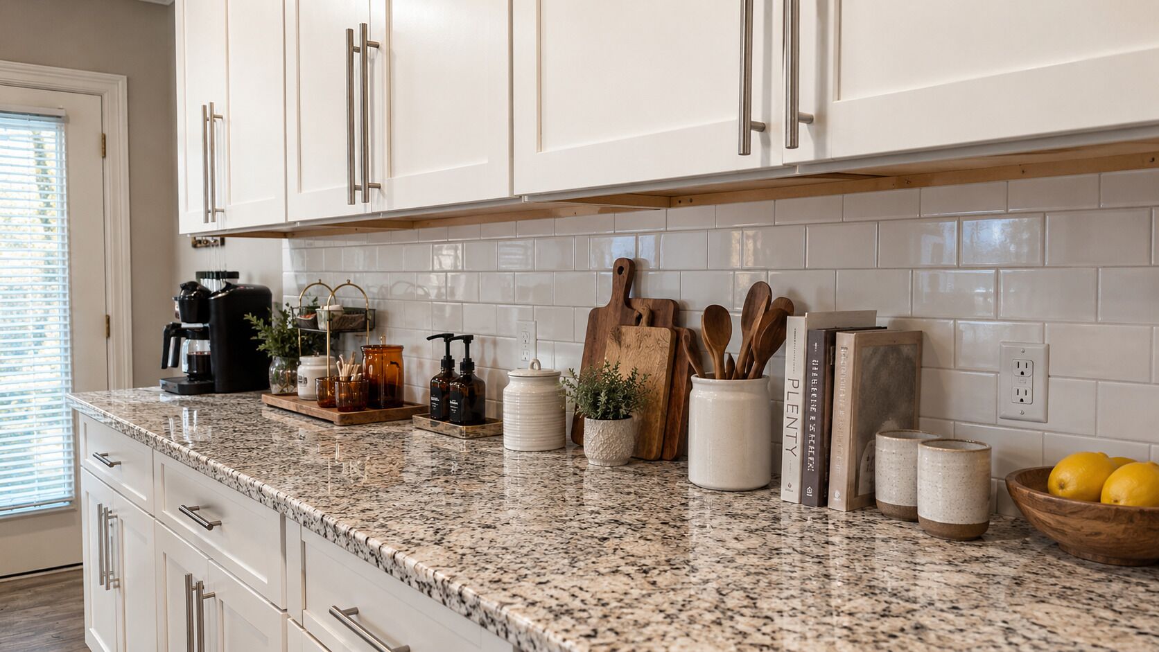 A kitchen with white cabinets, a granite countertop, and various kitchen items.