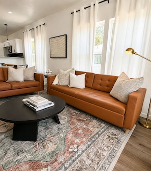 Ein modernes Wohnzimmer mit einem braunen Ledersofa, einem Couchtisch und einem gemusterten Teppich.