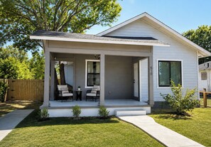 A modern single-story house with a covered porch, a small garden, and a wooden fence. - Historic luxury bungalow downtown + fenced yard (San Antonio)