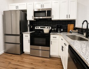 A modern kitchen with stainless steel appliances, white cabinetry, and a black tiled backsplash. - Historic luxury bungalow downtown + fenced yard (San Antonio)