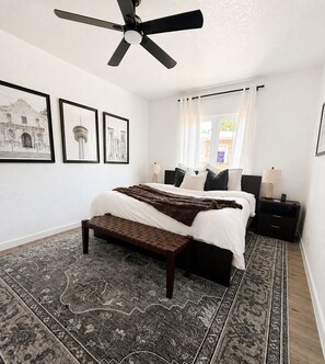 Ein Schlafzimmer mit einem Bett, Nachttischen, einem Deckenventilator und einem gemusterten Teppich.
