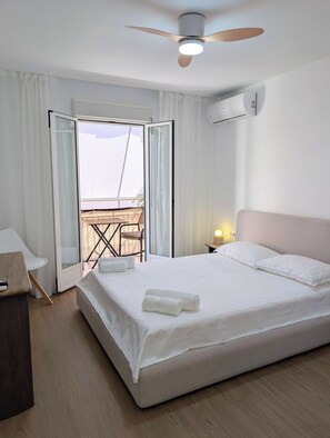 Ein Hotelzimmer mit einem Bett, einem Schreibtisch, einem Stuhl, einem Deckenventilator, einer Klimaanlage und Blick ins Freie.