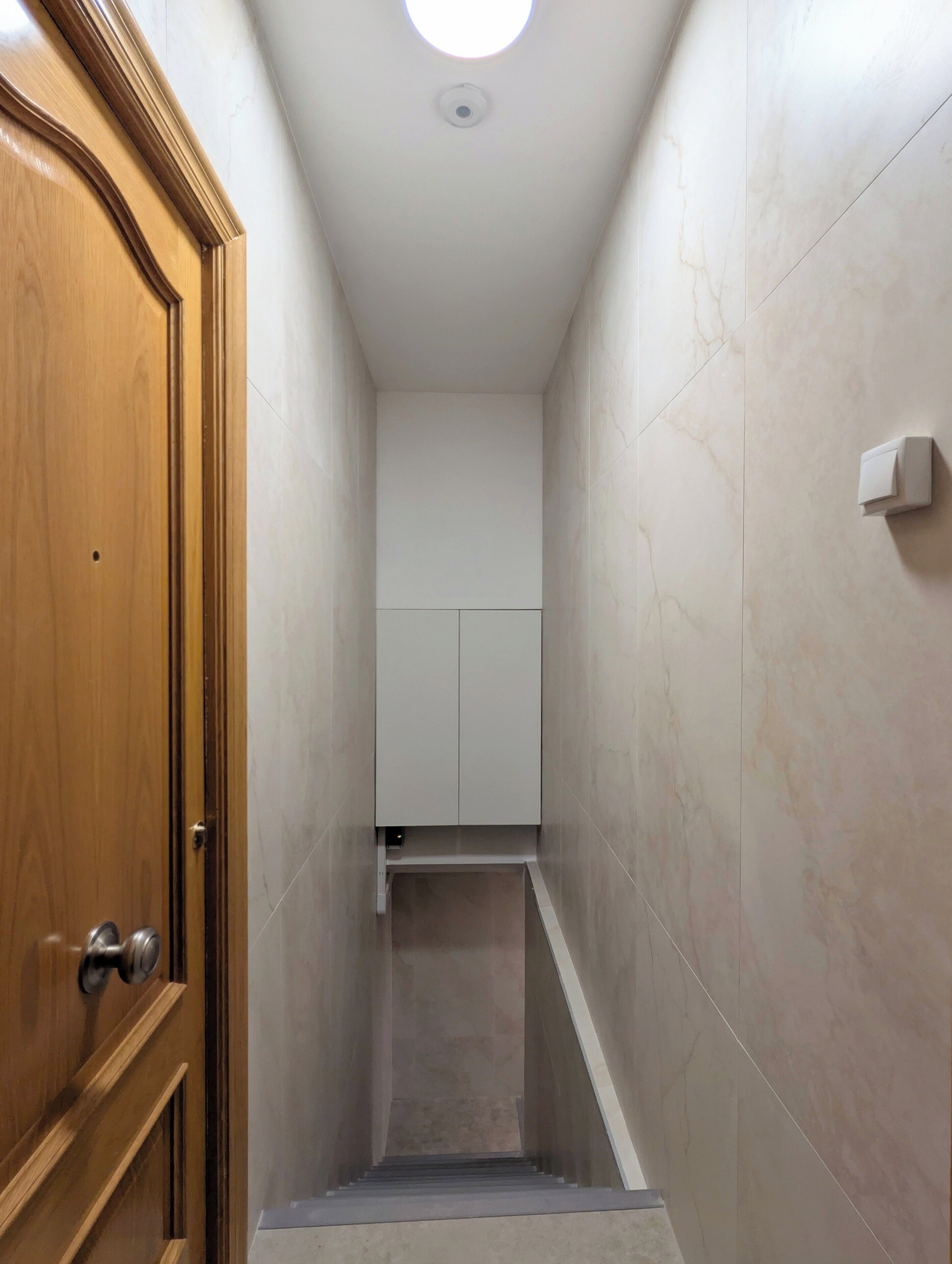 Ein schmaler Korridor mit einer Holztür links und einem weißen Schrank in der Mitte.