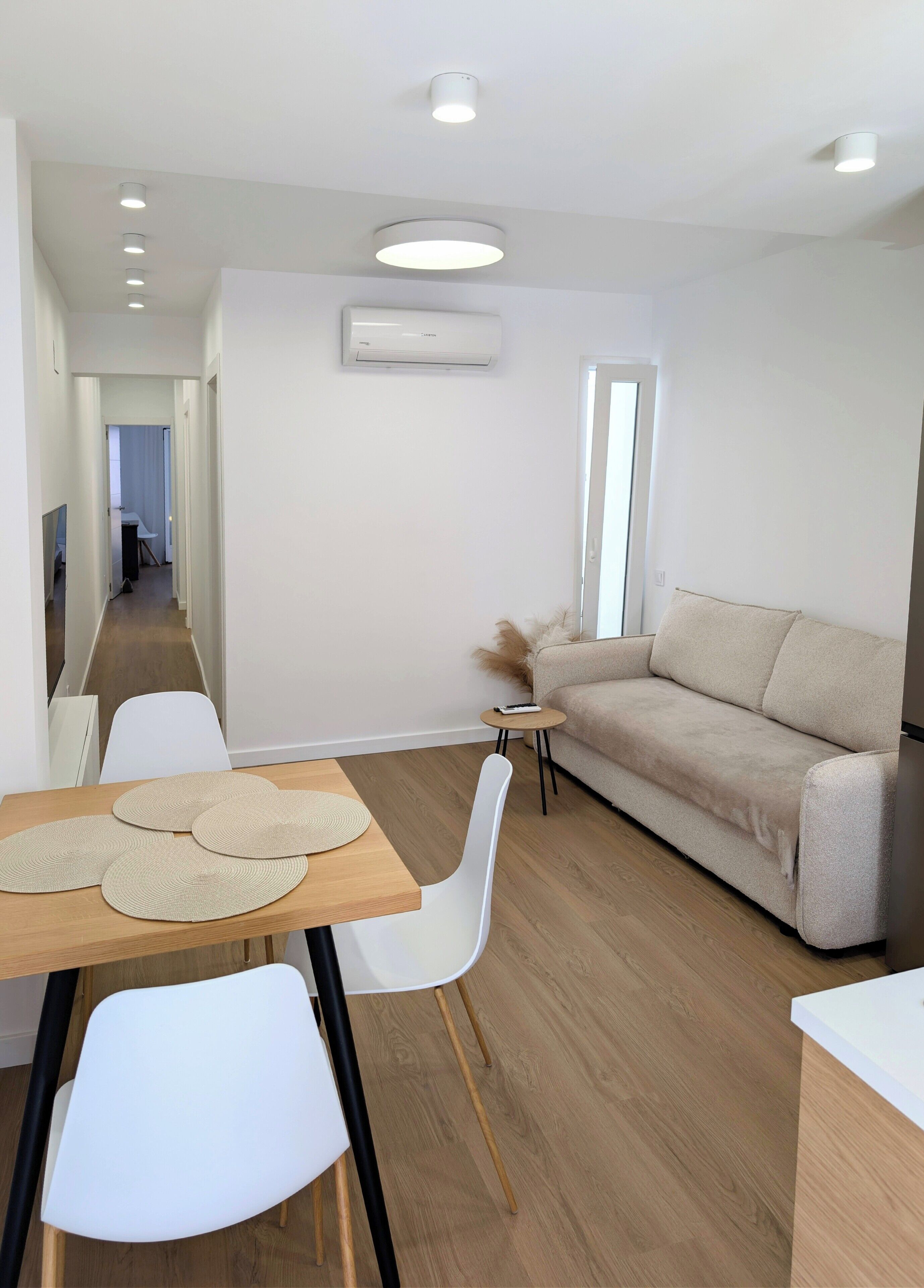 Una sala moderna con un sofá, una mesa de comedor con sillas y una mesita auxiliar con un control remoto.