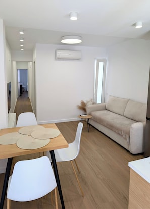 Ein modernes Wohnzimmer mit einer Couch, einem Esstisch mit Stühlen und einem kleinen Beistelltisch mit Fernbedienung.
