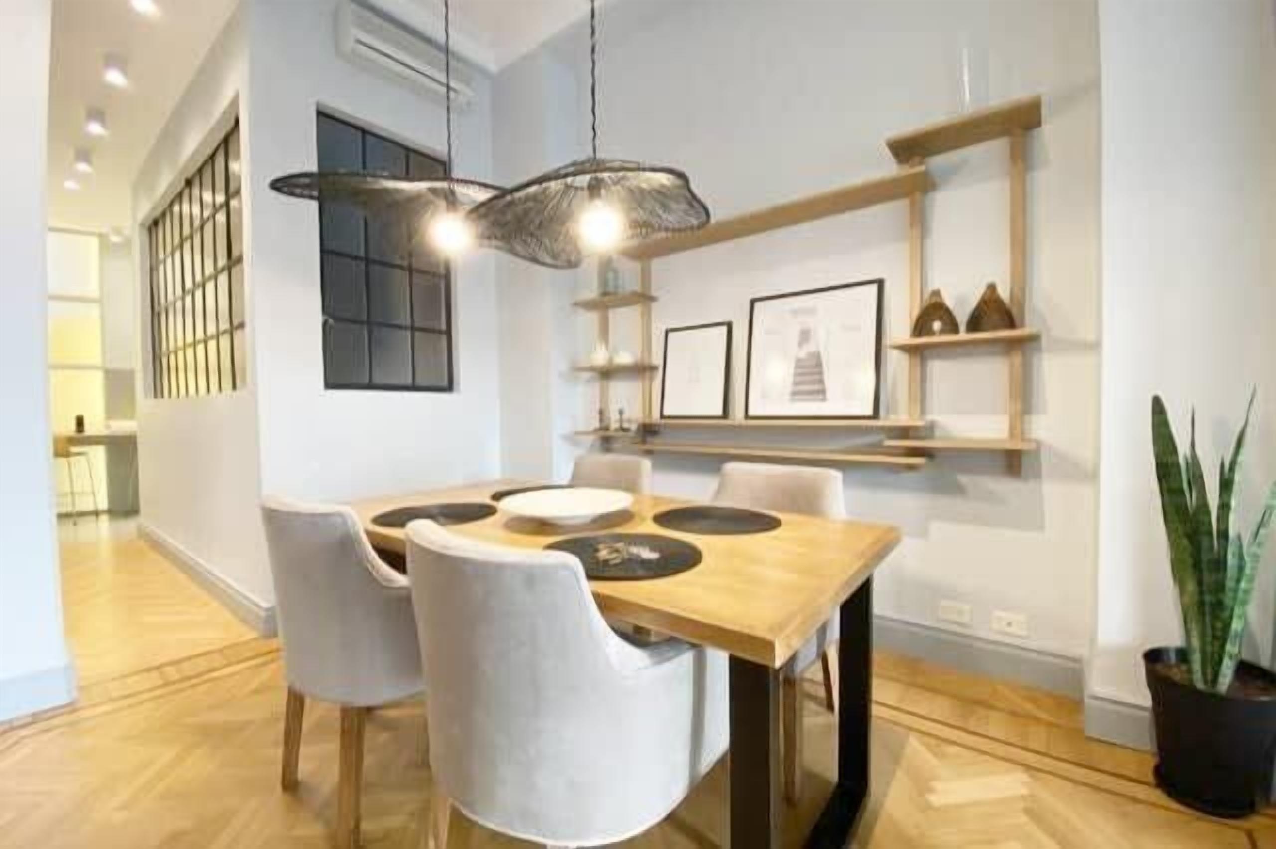 A dining area with a wooden table, chairs, pendant lighting, and a potted plant.