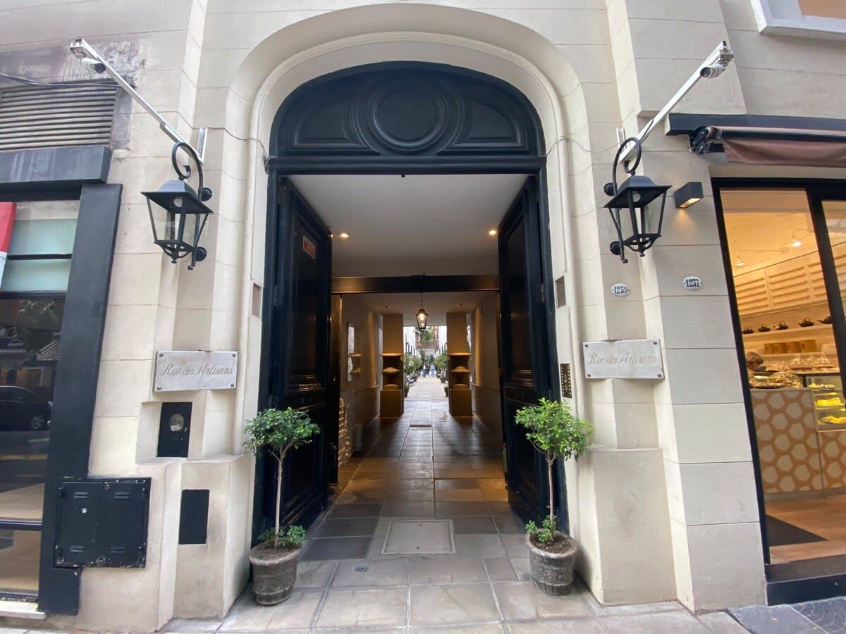 An entrance to a building with a black archway, potted plants, and a sign that reads 'Rue des Artisans.'