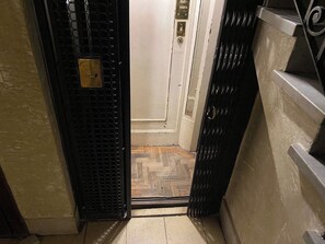 A narrow hallway with a door leading to a room. The door has a metal grille and a keyhole. The hallway has a tiled floor and walls painted in a light color. - 10- Incredible Apt. Privileged Location Recoleta (Buenos Aires)