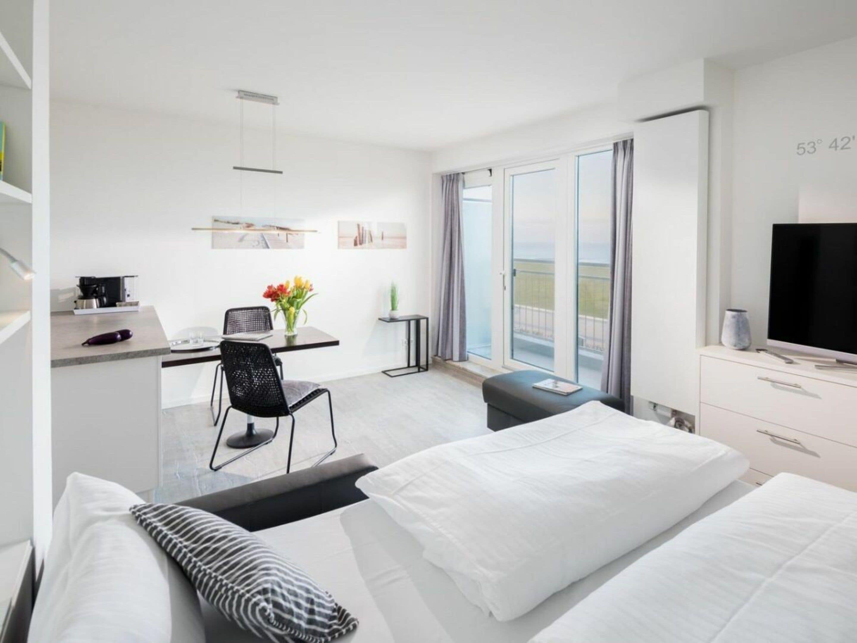 A modern hotel room with a bed, a desk with a chair, a television, and a balcony with a view.