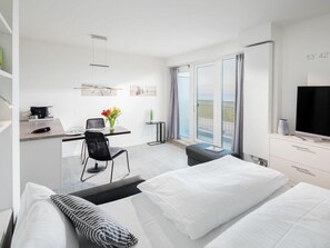 A modern hotel room with a bed, a desk with a chair, a television, and a balcony with a view. - Holiday Apartment in Norderney With Sauna (Norderney)