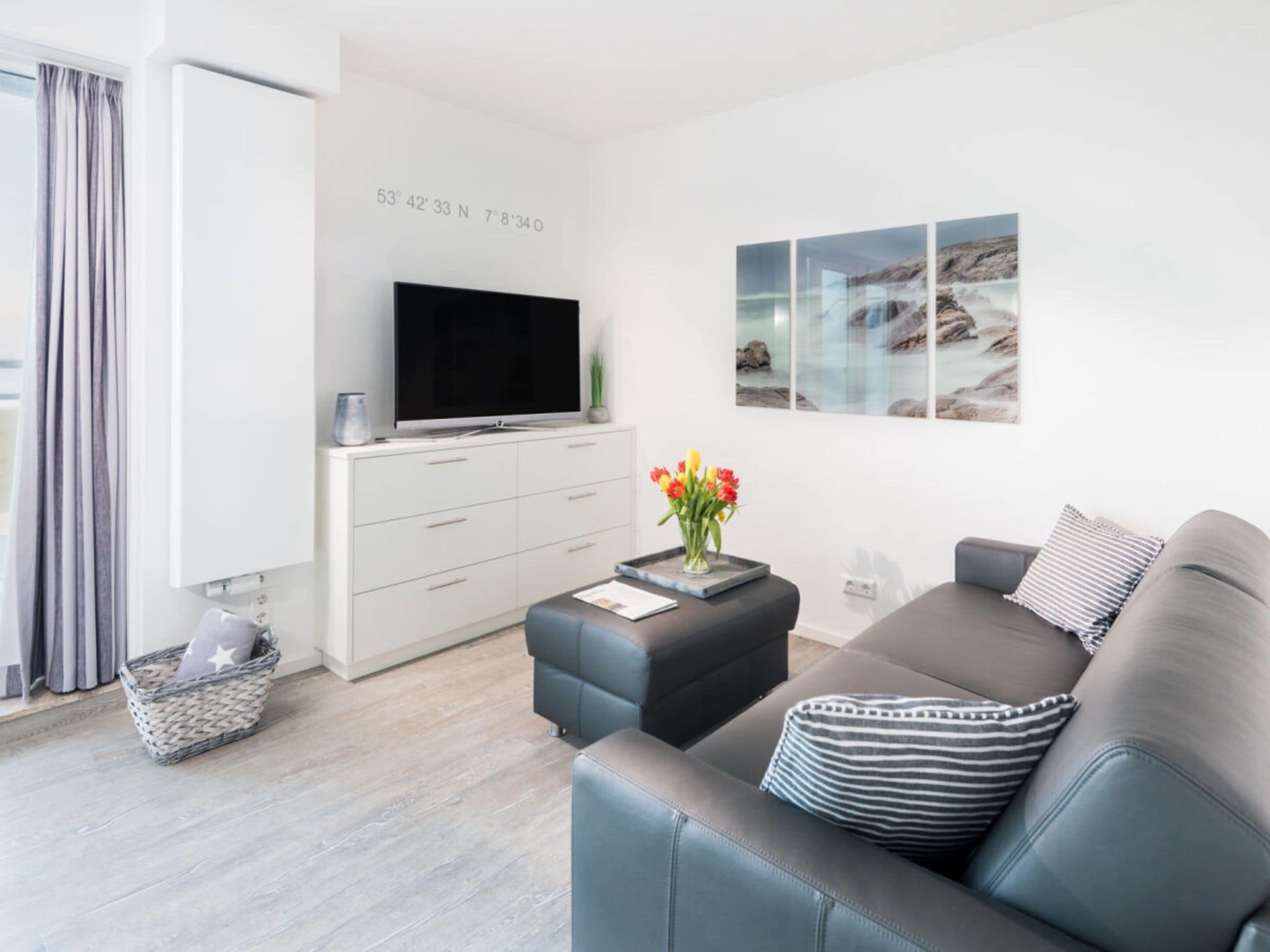 A modern living room with a flat-screen TV, grey sofa, and a wall-mounted artwork.