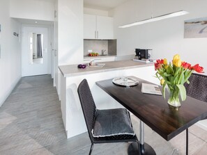 A modern kitchen with white cabinets, a central island, and a dining area with a dark wooden table and chairs. - Holiday Apartment in Norderney With Sauna (Norderney)