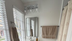 Ein Badezimmer mit einem weißen Waschbecken, einem Spiegel, einer Toilette, einem Handtuchhalter und einem Fenster mit Jalousien.