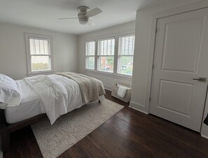 A bedroom with a bed, a ceiling fan, a window with blinds, a door, and a small basket by the window. - 3-bedroom duplex in Dundee Omaha (Omaha)