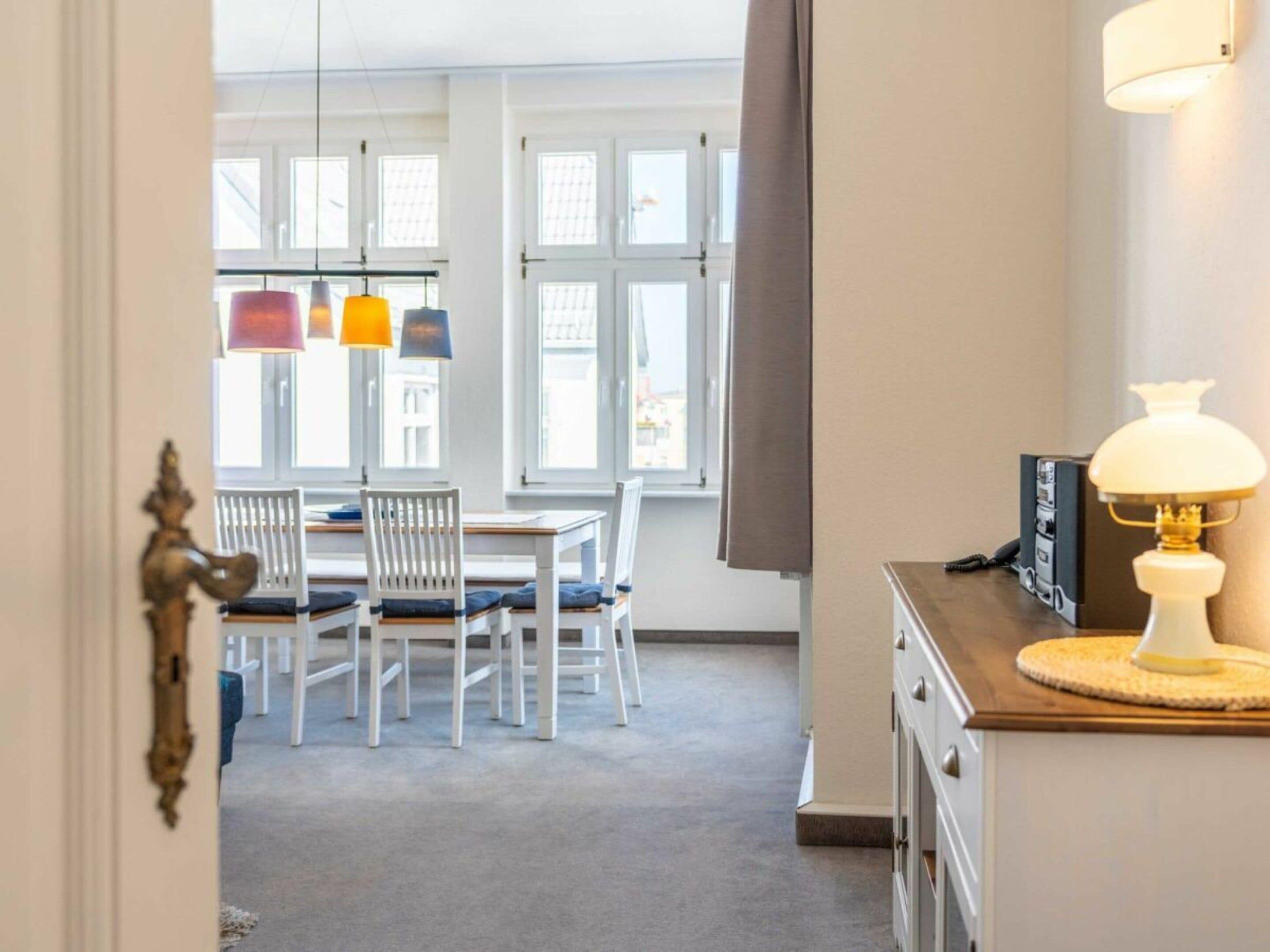 Una habitación con una mesa de comedor, sillas, una lámpara y vistas a través de una ventana.