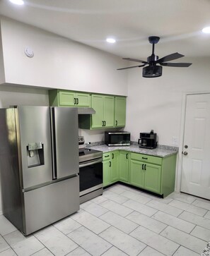 A kitchen with green cabinets, stainless steel appliances, a ceiling fan, and a white door. - Current River Home with Private River Access (Doniphan)