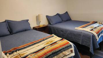 Une chambre avec deux lits, chacun recouvert d’une courtepointe bleue et agrémenté d’oreillers, une table de chevet avec une lampe et un ventilateur de plafond.