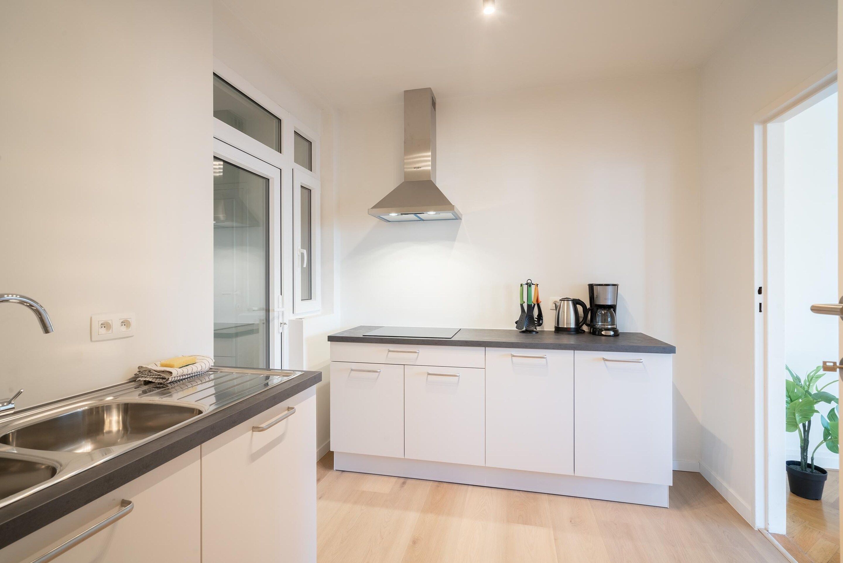 A modern kitchen with a stainless steel sink, a built-in oven, a range hood, and a countertop with a coffee maker.