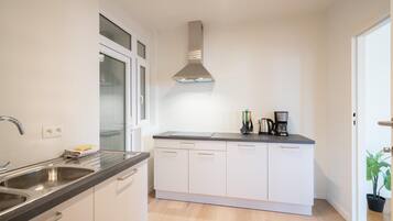 A modern kitchen with a stainless steel sink, a built-in oven, a range hood, and a countertop with a coffee maker.