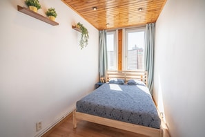 Un dormitorio con techo de madera, una cama con colcha estampada, dos mesitas de noche y una ventana con cortinas.