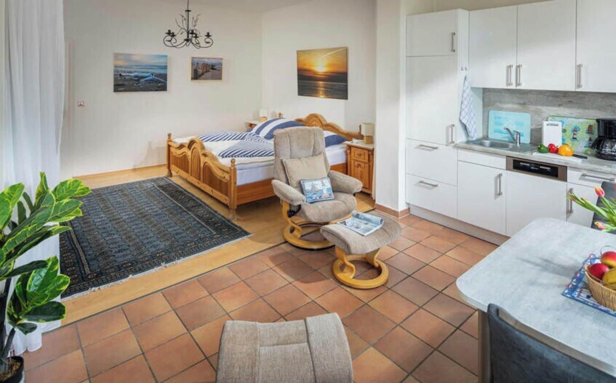 A bedroom with a bed, a chair, a bedside table, and a nightstand. There is a window with a view of the sea.