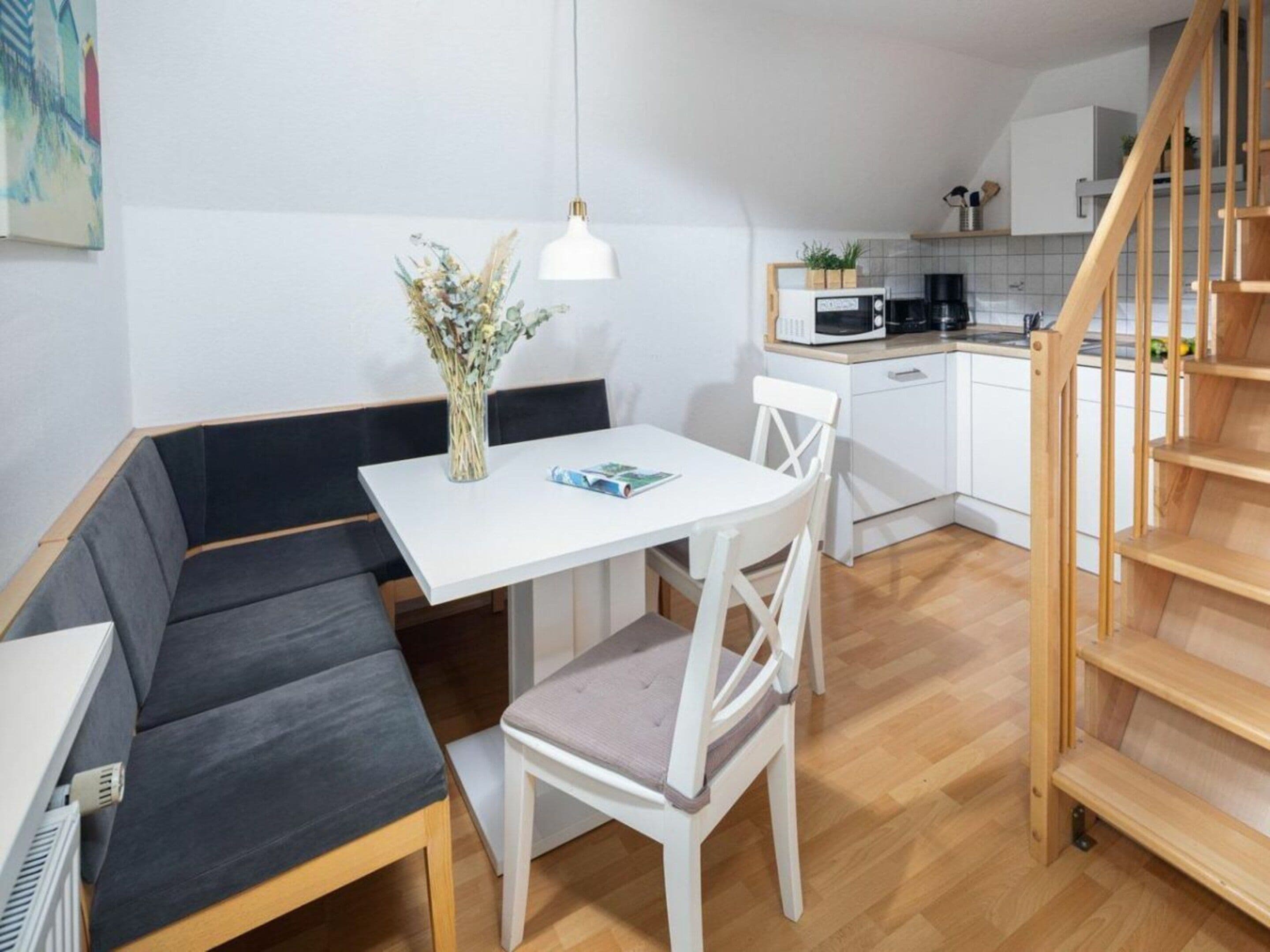 Eine moderne Küche mit weißen Schränken, einer Mikrowelle und einer Holztreppe.