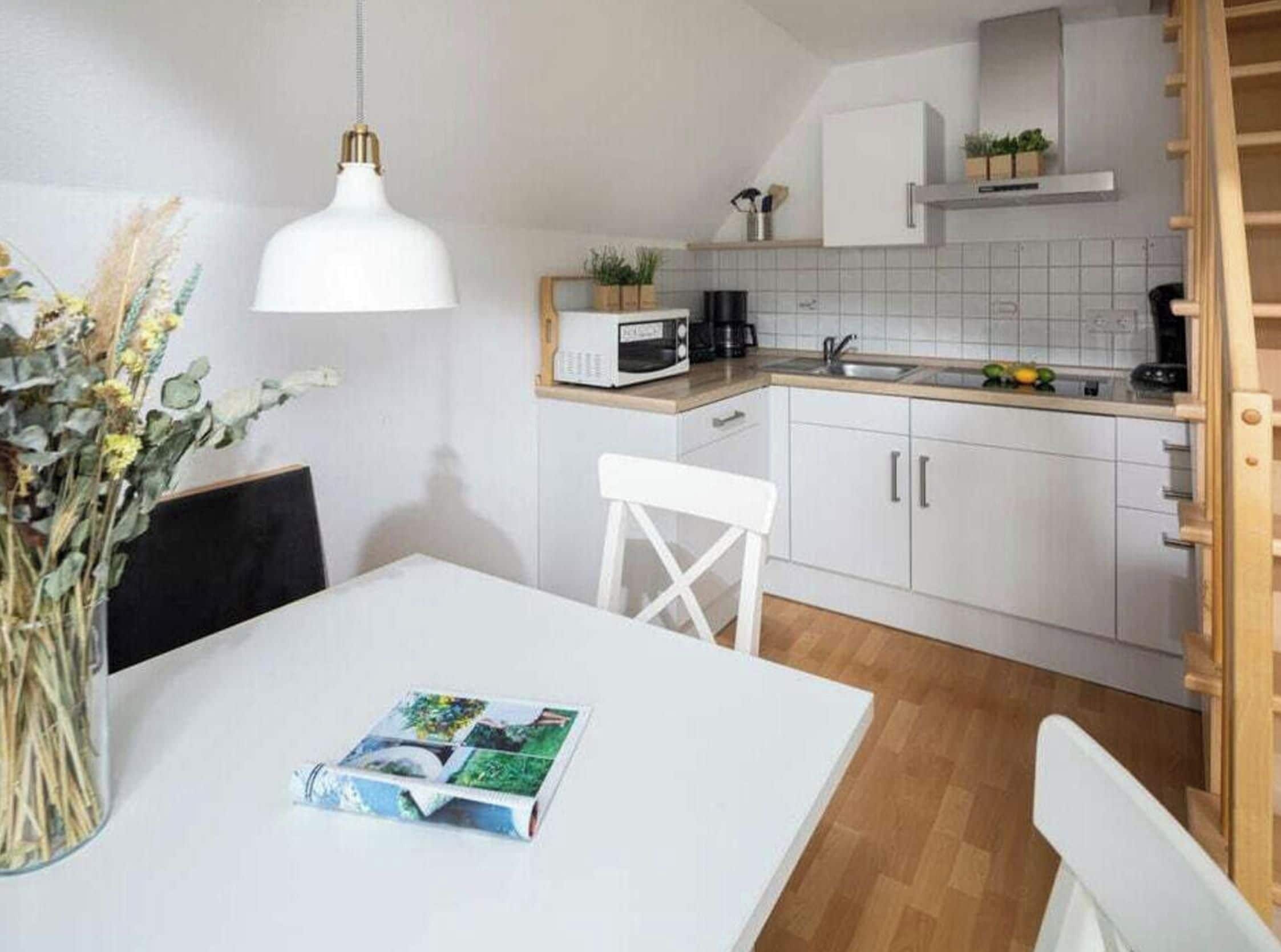 A modern kitchen with white cabinets, a white dining table, and a hanging light fixture.