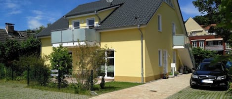 A two-story residential building with a sloped roof, a satellite dish, and a paved driveway.