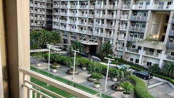A balcony with a view of a residential building, a green sports court, and a parking area.
