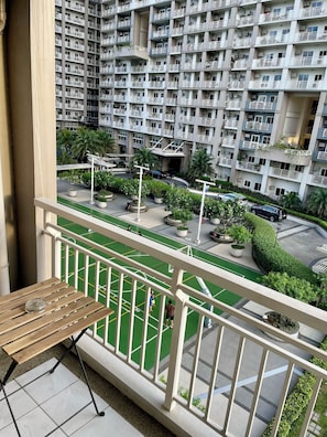 A balcony with a view of a residential building, a green sports court, and a parking area. - Lumiere Residences, Bright Large 2BR Condo w Balcony in Pasig (Pasig)