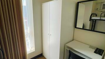 A room with a wardrobe, a desk, a chair, a potted plant, and a window with curtains.