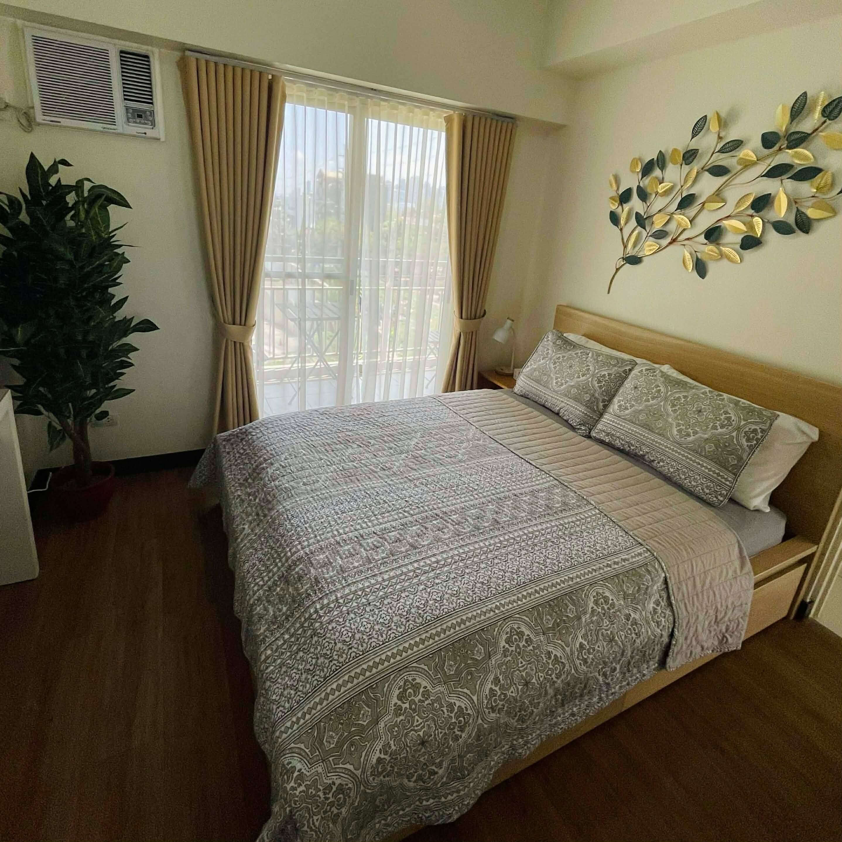 A bedroom with a bed, curtains, a wall-mounted plant, and a window with blinds.