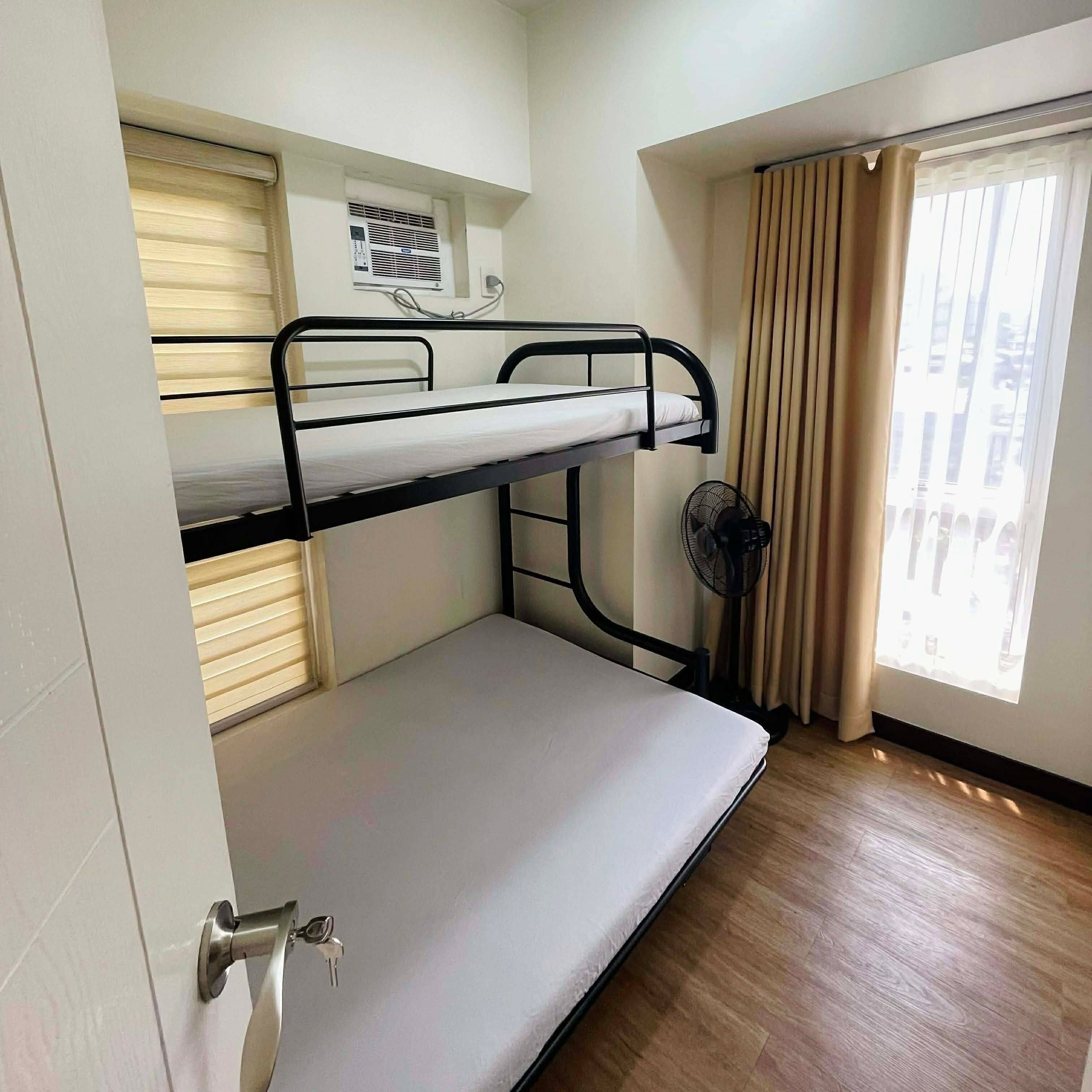 A bunk bed room with a window, a fan, and a door.
