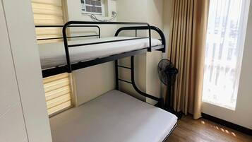 A bunk bed room with a window, a fan, and a door.