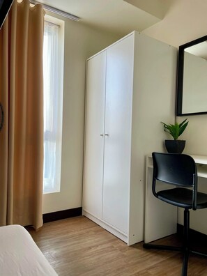 Una stanza con un letto, un armadio, una scrivania con una sedia, una pianta in vaso e una finestra con tende.