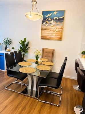 A dining area with a glass table, black chairs, woven placemats, a painting, and a pendant light. - Fabulous 4-bedroom house with 3 full bath l ACs in all rooms l Sleeps 8 plus  (Calgary)