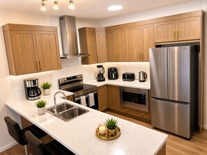 A modern kitchen with stainless steel appliances, wooden cabinets, and a central island with seating. - Fabulous 4-bedroom house with 3 full bath l ACs in all rooms l Sleeps 8 plus  (Calgary)