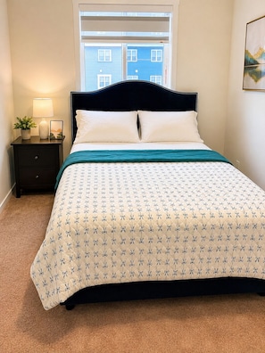 A bedroom with a bed, a nightstand, a lamp, and a window with a view of buildings. - Fabulous 4-bedroom house with 3 full bath l ACs in all rooms l Sleeps 8 plus  (Calgary)