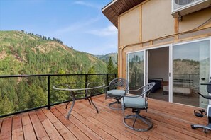A wooden deck with a table and chairs, overlooking a mountainous landscape.