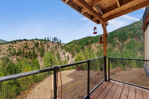 A wooden deck with a metal railing overlooking a mountainous landscape.
