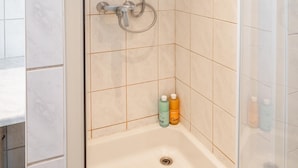 Una ducha a nivel con puerta de cristal, cabezal de ducha de mano y rociador de mano.