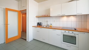 Una cocina moderna con armarios blancos, una encimera de madera, horno empotrado y una lámpara colgante.