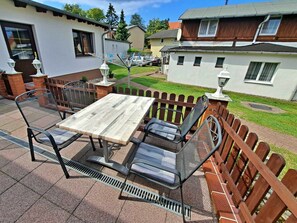 An outdoor patio with a wooden table and metal chairs, surrounded by a brick wall and a wooden fence. - Groth Holiday Apartments (Heringsdorf)